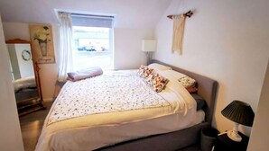 Un dormitorio con cama, lámpara de noche, ventana con cortinas, lámpara de pared y un adorno en la pared.