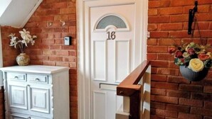 Una puerta blanca con el número 16, un armario blanco y una pared de ladrillo con una cesta colgante de flores.