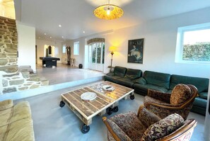 A spacious living area with a pool table, green sofas, and a unique coffee table.
