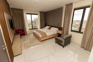 A modern hotel room with a large bed, a sofa, a TV, and a view of the city.