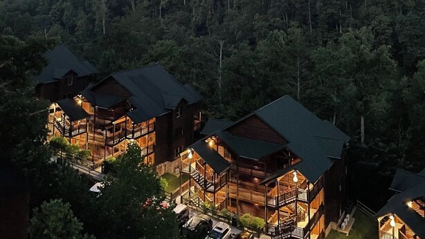 Eine Lodge mit mehreren Holzhäusern, umgeben von dichtem Wald und einem nebelverhangenen Hügel im Hintergrund.