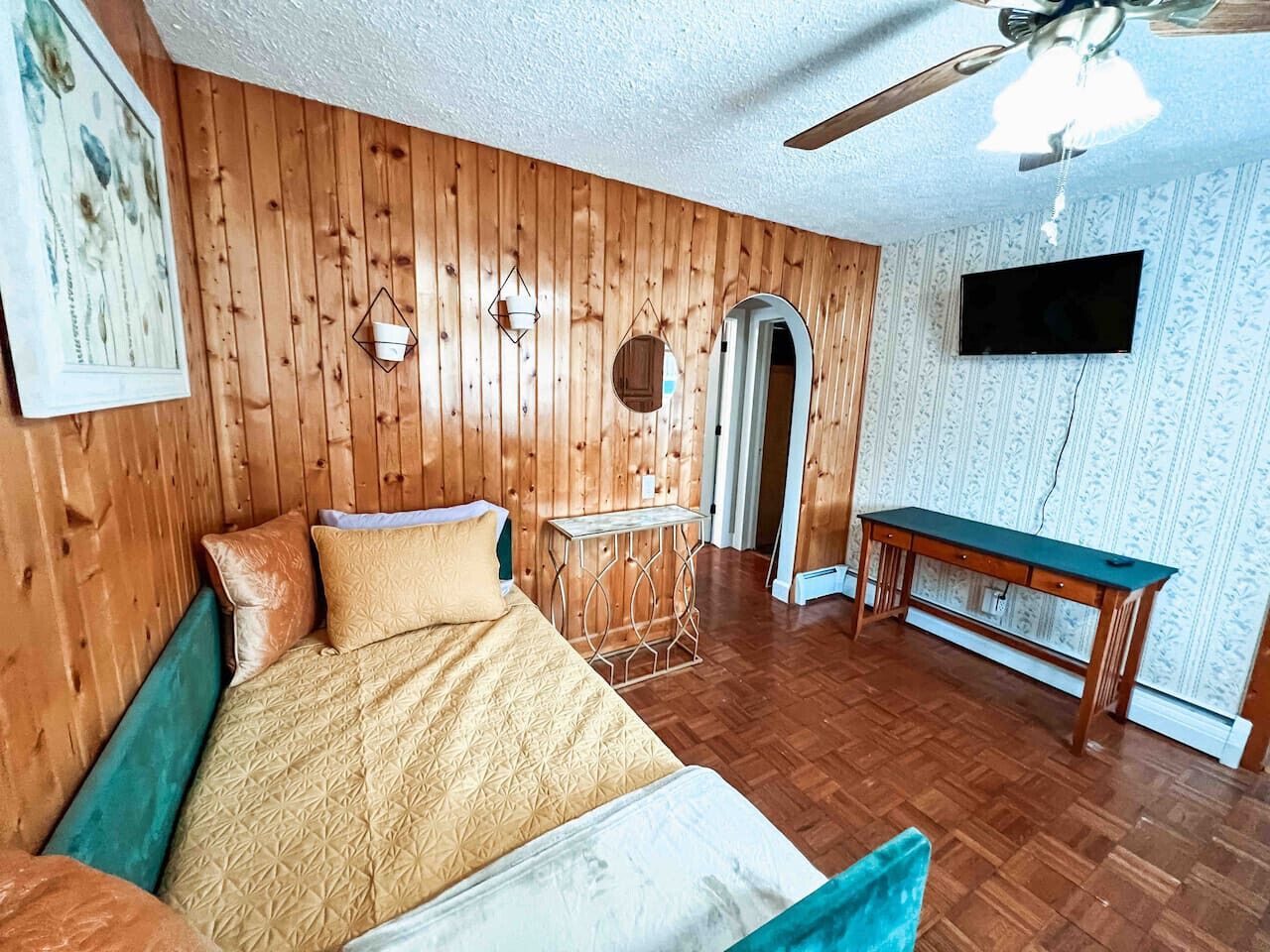 Una habitació amb un llit, parets de fusta, una televisió i un escriptori.