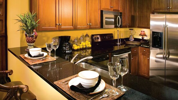 Una cocina con armarios de madera, electrodomésticos de acero inoxidable y un comedor con una mesa dispuesta para dos.