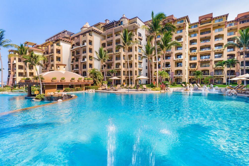 Un hotel con una grande piscina, palme e un edificio a più piani con balconi.