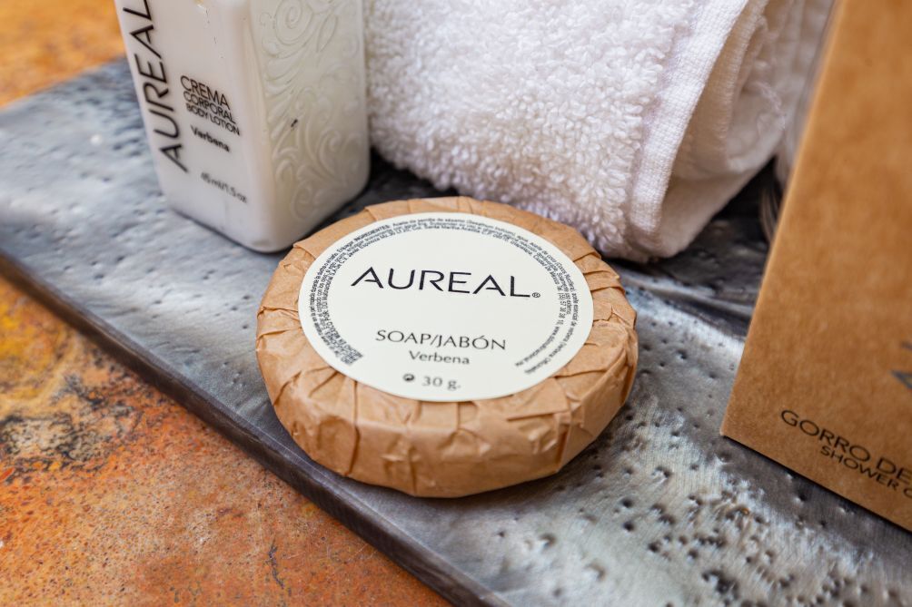 Eine Seife von Aurel, eine weiße Flasche Aurel Body Lotion und eine braune Papiertüte mit dem Aufdruck 'Gorro de Shower'.
