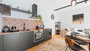 A modern kitchen with a brick backsplash, integrated appliances, and a dining area with a wooden table and chairs. - The Industrialist – Design Suite in Central Vienna (Vienna)