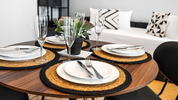 A round dining table with black and gold placemats, white plates, silverware, and clear glasses. - The Industrialist – Design Suite in Central Vienna (Vienna)