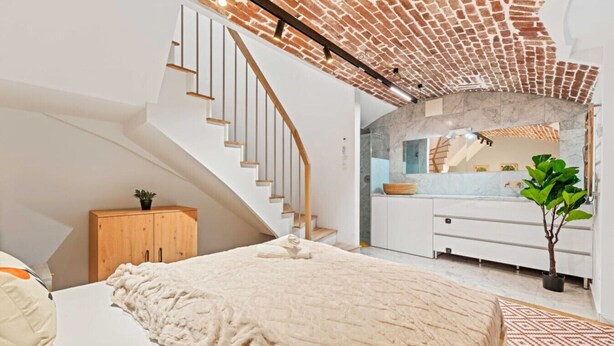 Une chambre avec un plafond en pente, un escalier en bois, un lit, une coiffeuse avec un miroir et une plante en pot.