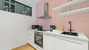 A compact kitchen with white cabinetry, a built-in oven, a microwave, a coffee maker, and a sink with a modern faucet.