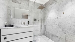 A modern bathroom with a marble wall, a glass-enclosed shower, and a white vanity with a mirror.