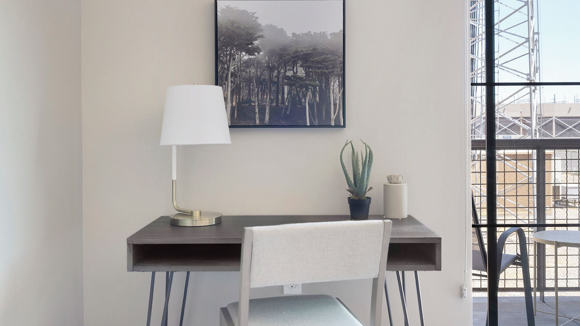 A modern workspace with a desk, chair, lamp, and a framed picture of trees.