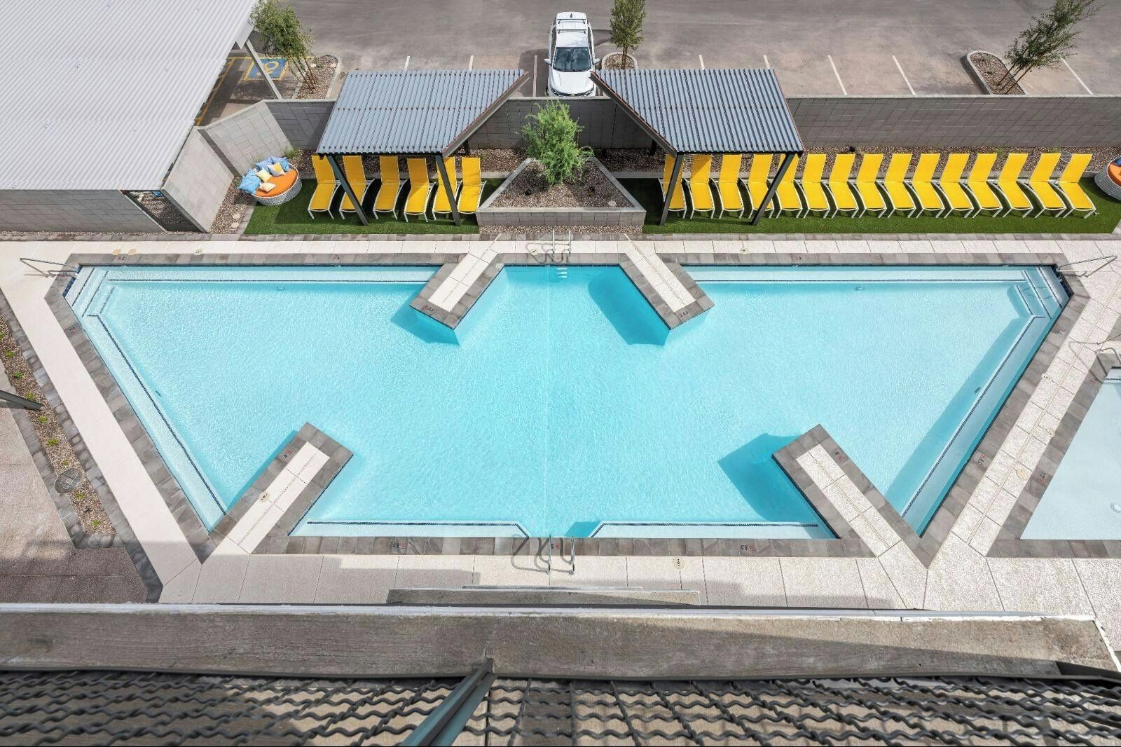 Ein rechteckiger Pool mit gefliestem Sonnendeck, umgeben von gelben und schwarzen Liegestühlen.