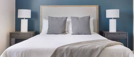 A neatly made bed with a patterned throw, two bedside lamps, and a headboard against a blue wall.