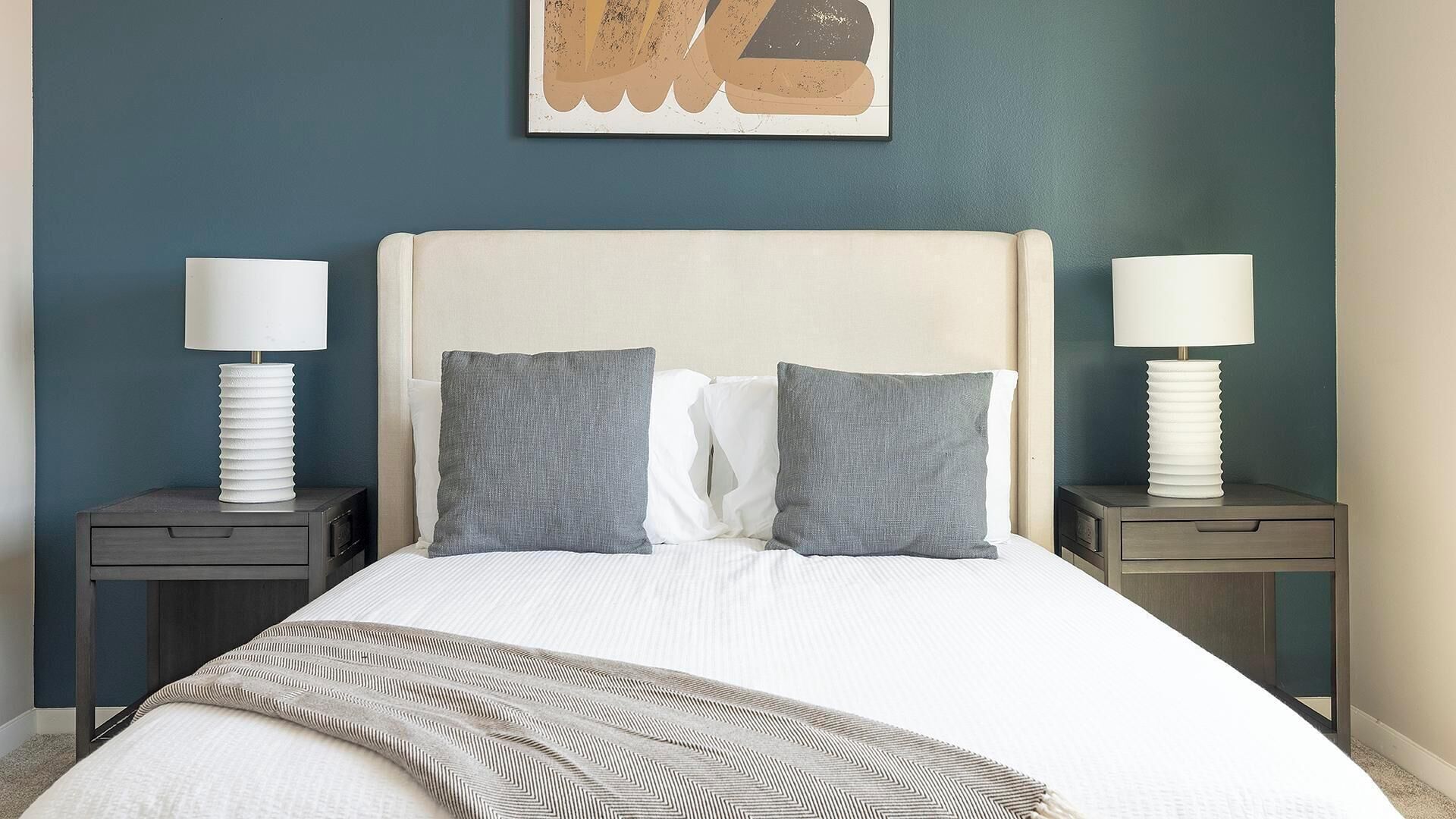 A neatly made bed with a white headboard, two bedside tables with lamps, and a gray throw blanket.