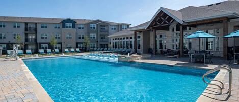 A swimming pool with lounge chairs and umbrellas, surrounded by multi-story buildings with balconies.