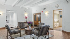Un vestíbulo amplio con piso de ladrillo, una zona de estar central con sillones acolchados, una mesa redonda y un florero con flores.