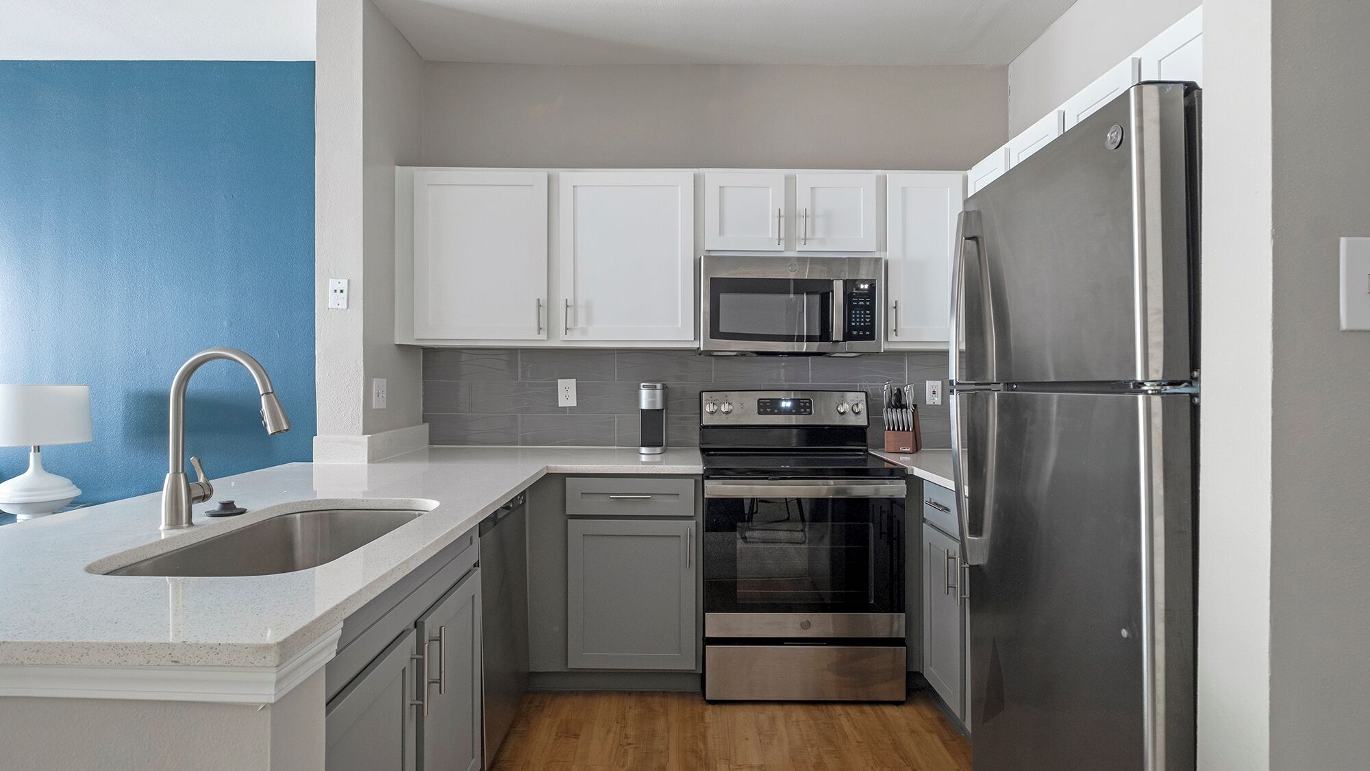 A modern kitchen with stainless steel appliances, white cabinets, and a blue accent wall.