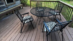 Een houten terras met een ronde tafel en vier stoelen, omgeven door een houten hek en bomen.