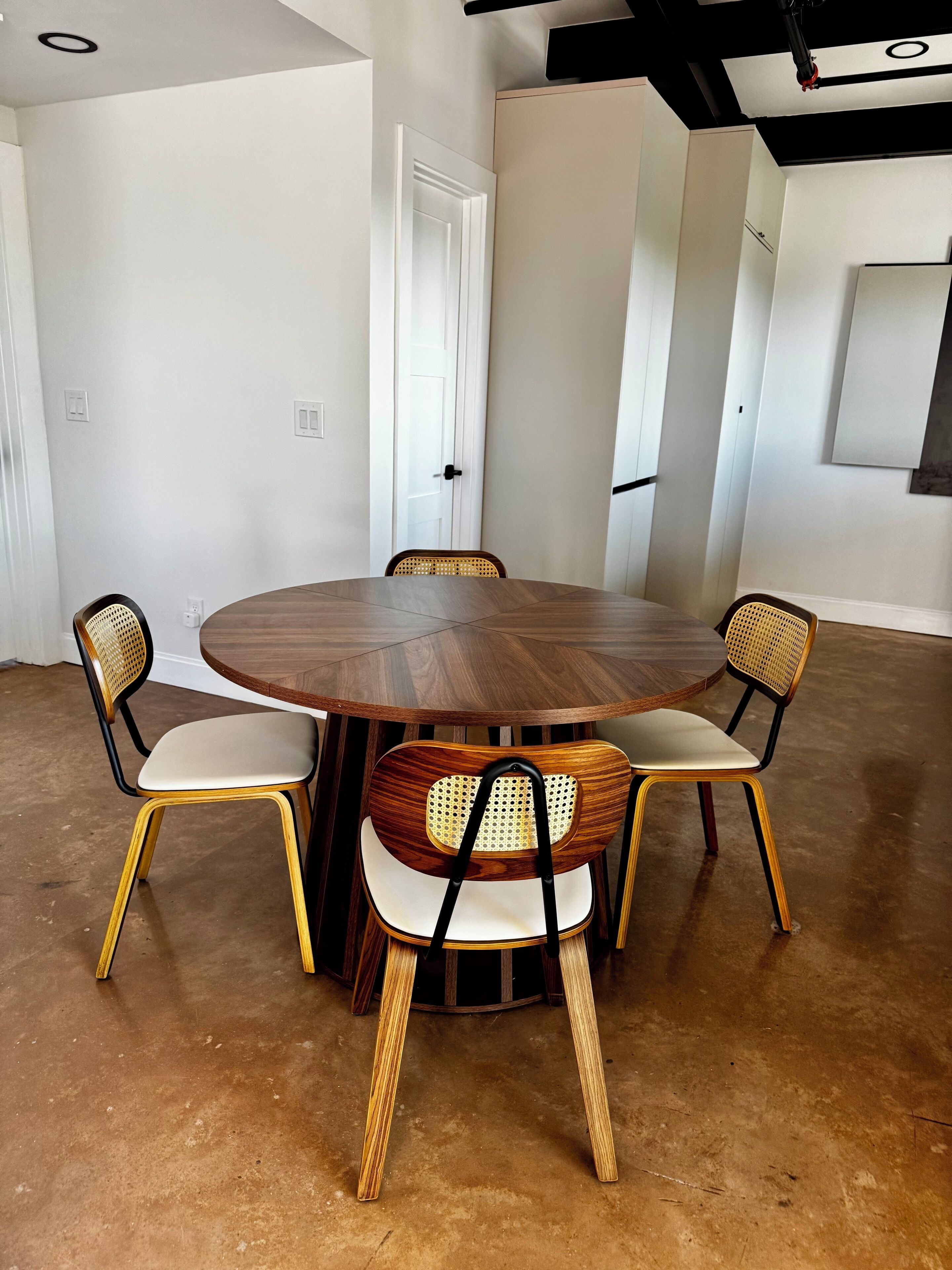 Une table de salle à manger ronde en bois, entourée de quatre chaises dont les dossiers et les assises sont en tissu tissé et rembourrés.