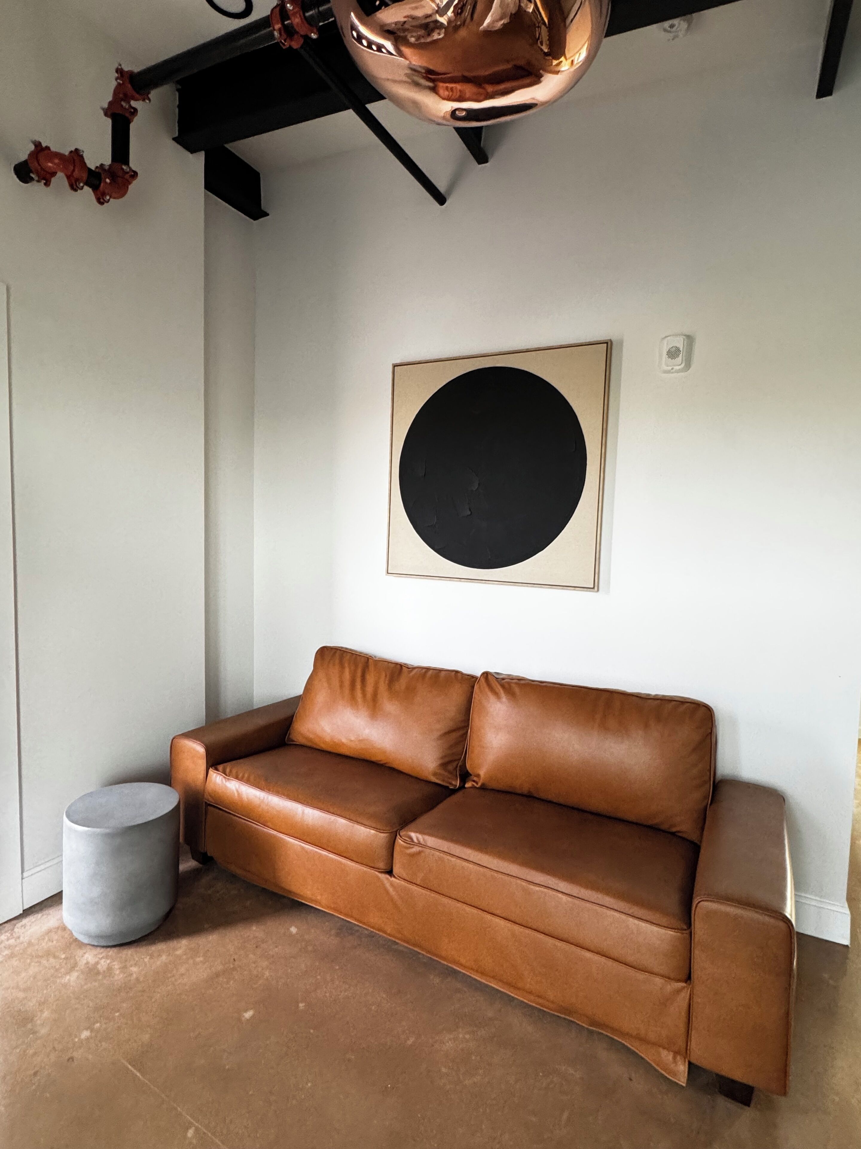 A brown leather sofa against a white wall with a large black circle artwork above it.