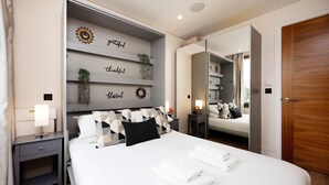 A modern bedroom with a bed, bedside tables, a mirror, and decorative wall art. - Luxury Apartment Near Notting Hill (London)