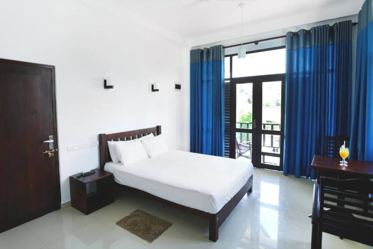 A bedroom with a bed, a nightstand, a table with a drink, and a view of the outdoors through a door.