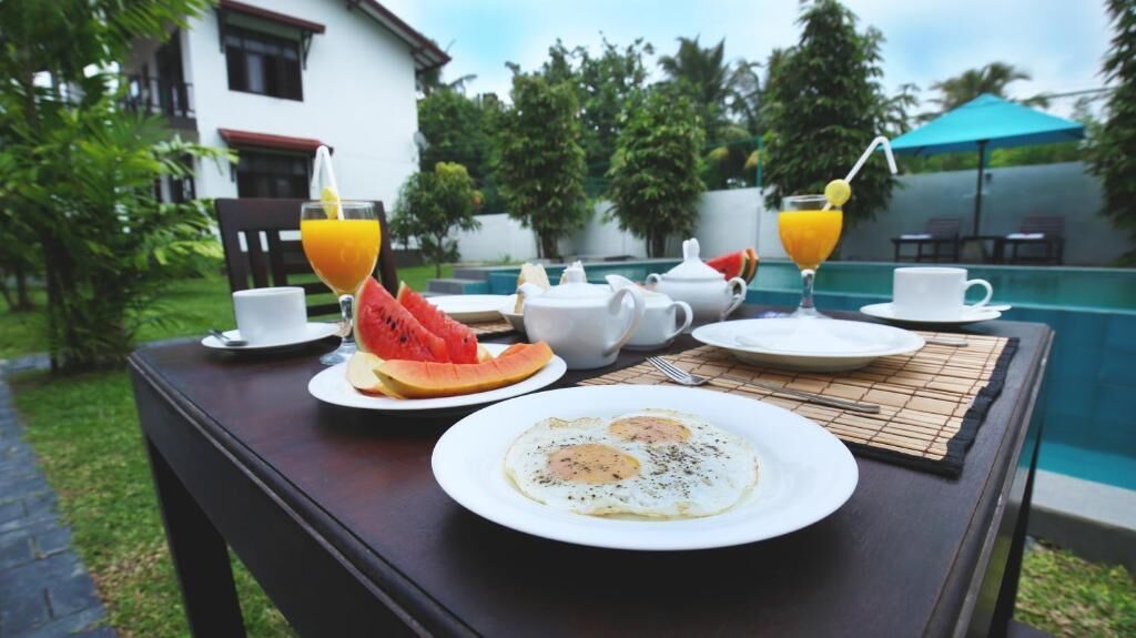 A breakfast setup with eggs, watermelon, and orange juice on a table by a pool.