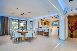 Une cuisine moderne dotée d’un îlot central, d’un coin repas avec une table ronde et des chaises, et offrant une vue dégagée grâce à de grandes fenêtres.