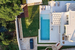 Une maison moderne avec une piscine, une voiture garée devant et une pelouse bien entretenue.