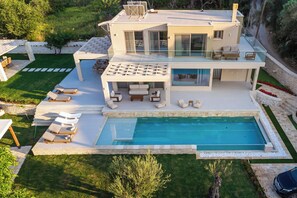 A modern two-story house with a swimming pool, outdoor seating, and a well-maintained garden.