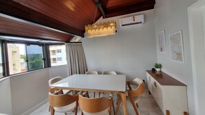 A dining area with a white table and wooden chairs, a ceiling fan, and a view of buildings through large windows.