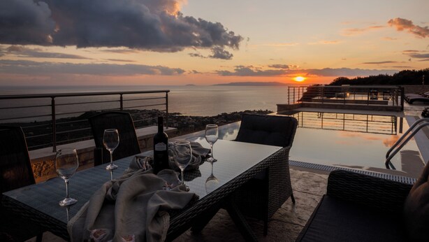 An outdoor dining area with a table set for two, overlooking a body of water and a sunset.
