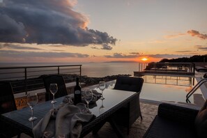 An outdoor dining area with a table set for two, overlooking a body of water and a sunset. - Manazil Mani Luxury Villas Estate.....
6 bedrooms estate with two private pools. (stoupa)