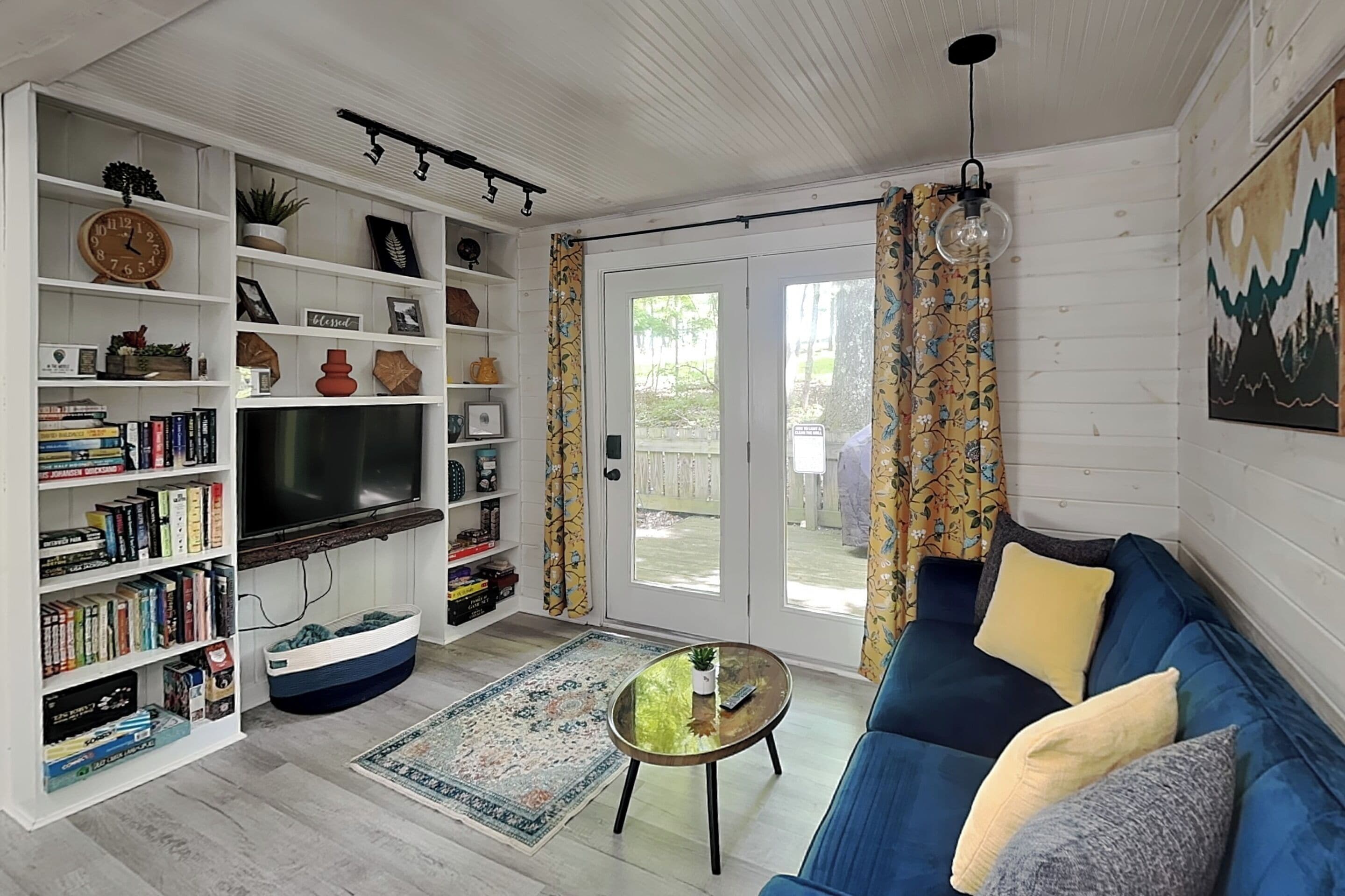 A living room with a TV, bookshelves, a sofa, a coffee table, and a patterned rug.