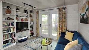 Una sala de estar con televisión, estanterías, un sofá, una mesa de centro y una alfombra estampada.