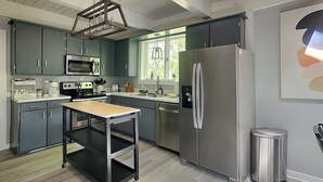 Una cocina moderna con armarios grises, electrodomésticos de acero inoxidable, una mesa de madera y una ventana con vistas a la vegetación.