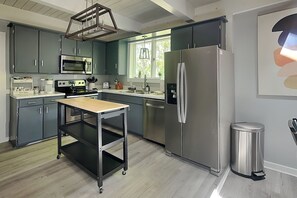 A modern kitchen with grey cabinets, stainless steel appliances, a wooden table, and a window with a view of greenery.