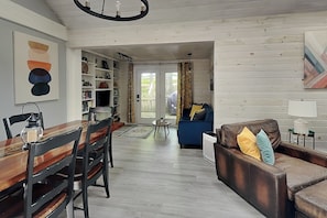 A spacious living area with a wooden dining table, a blue sofa, and a bookshelf.