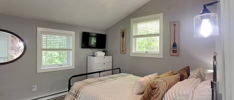 A bedroom with a bed, a ceiling fan, a TV, a dresser, and a window with blinds.