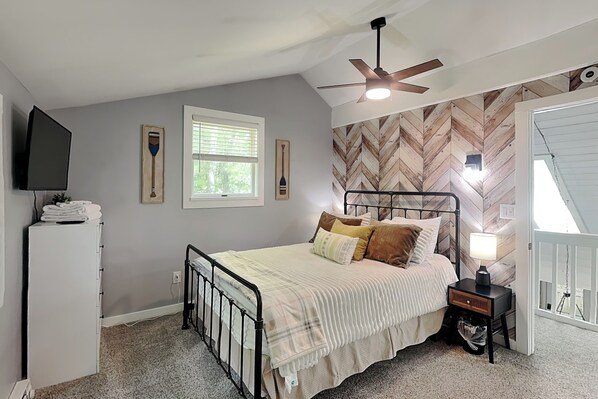 A bedroom with a bed, a ceiling fan, a TV, a window, and a herringbone-patterned wall.