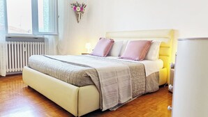 A bedroom with a bed, bedside lamps, a radiator, and a window.