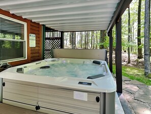 A hot tub in a covered outdoor area with a wooden cabin and a forest backdrop. - Campfire Lodge by Taylor Made Deep Creek (Swanton)