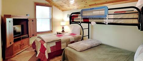 A room with wooden ceiling, bunk beds, a TV, and a window with blinds.