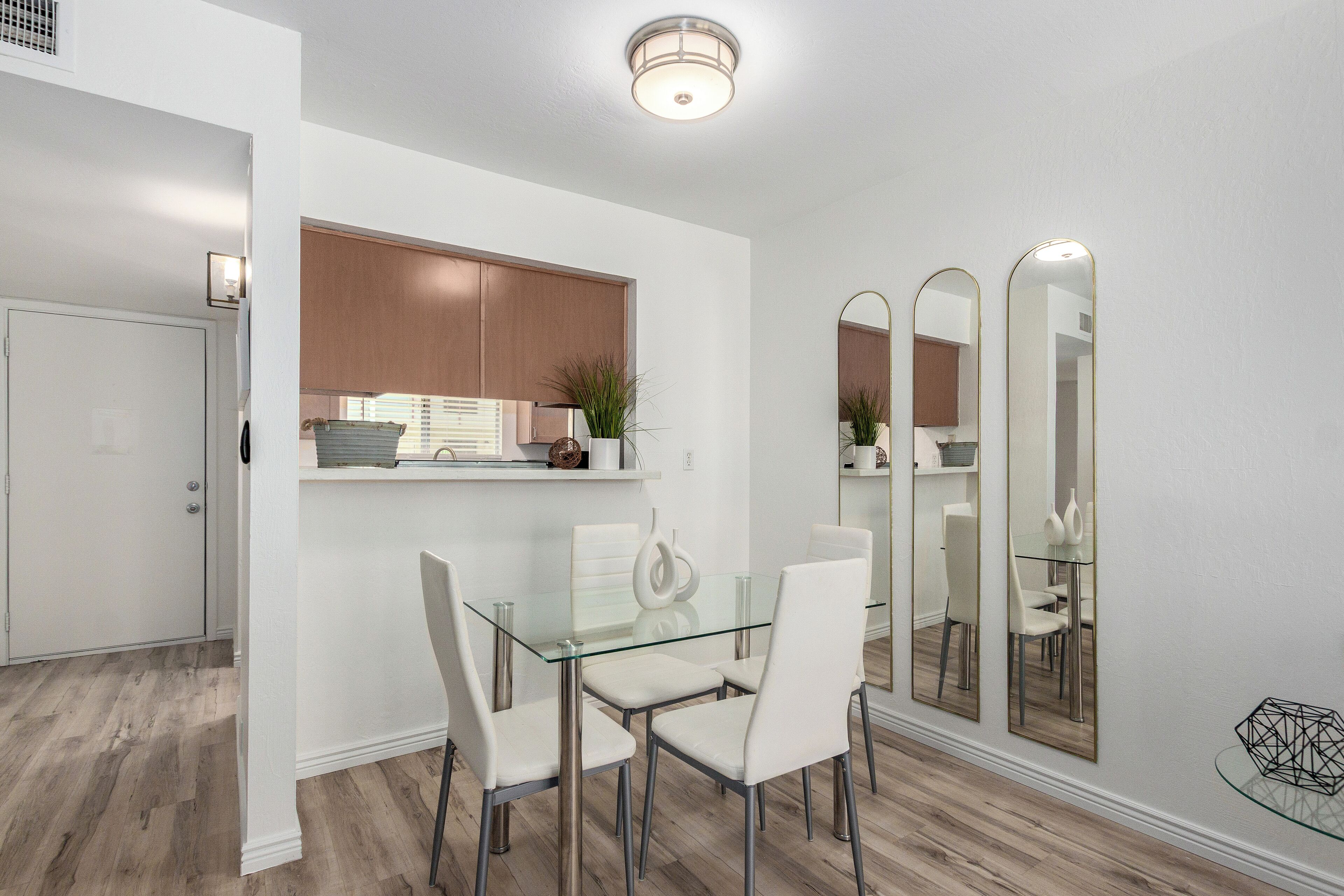 A modern dining area with a glass table and white chairs, a wooden cabinet, and a mirror on the wall.
