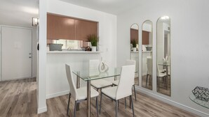 Un espace repas moderne avec une table en verre et des chaises blanches, un meuble en bois et un miroir au mur.