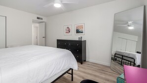 Une chambre à coucher avec un lit, une commode, un miroir et un ventilateur de plafond.