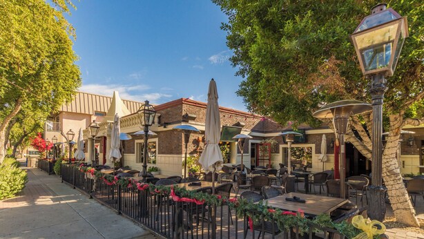 Un espace extérieur aménagé en terrasse, avec des tables et des chaises, dont certaines sont dotées de parasols, et une clôture décorative.