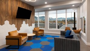 Un interior moderno con un ventanal grande, un televisor de pantalla plana y una zona de estar con alfombra azul estampada.