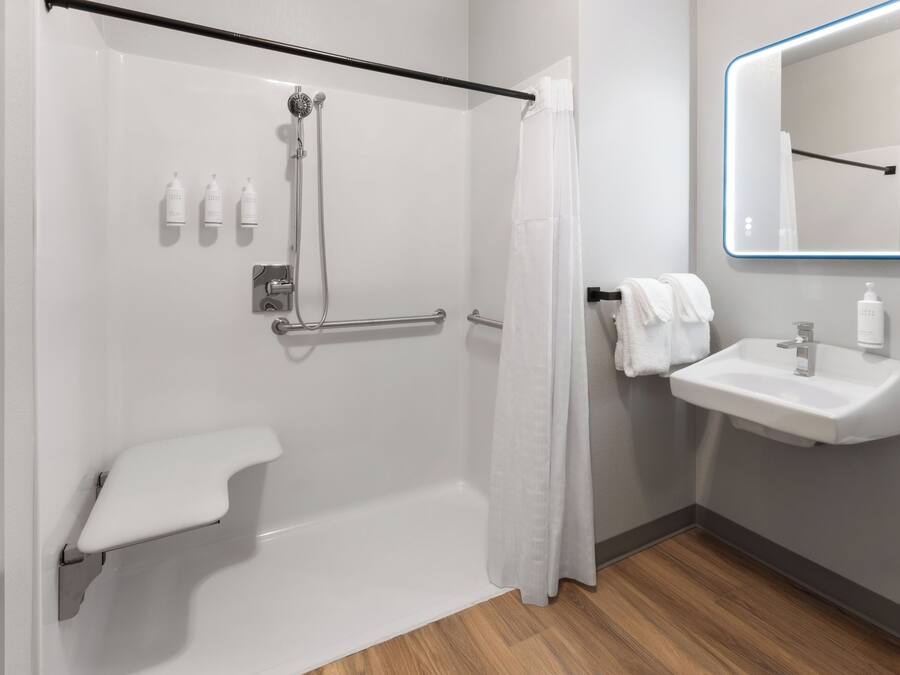 Un baño moderno con cabina de ducha, barra de apoyo, lavabo blanco y espejo con marco azul.