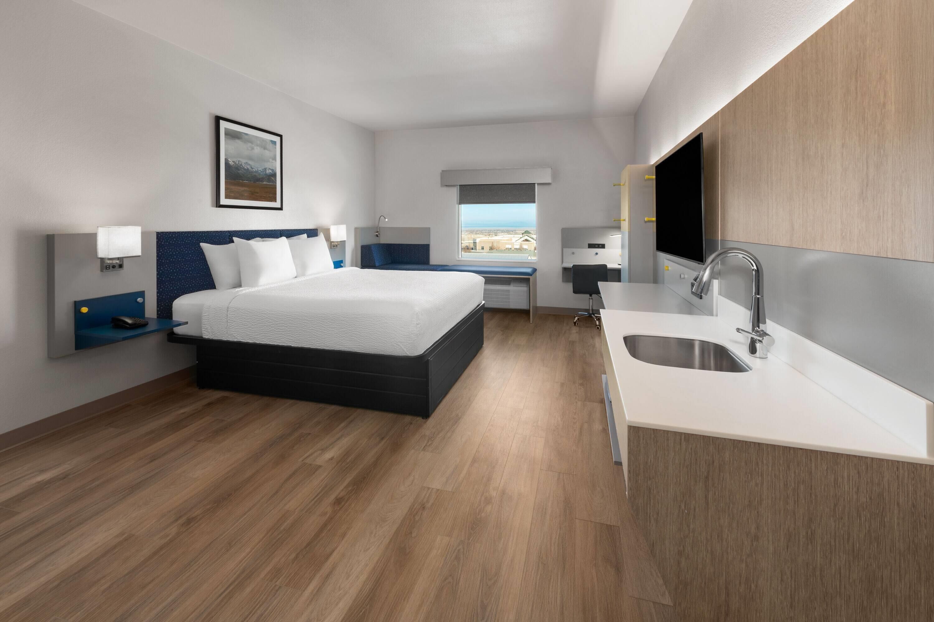 Ein modernes Hotelzimmer mit einem großen Bett, einem kleinen Schreibtisch, einer integrierten Spüle und einem Fenster mit Blick auf die Stadt.